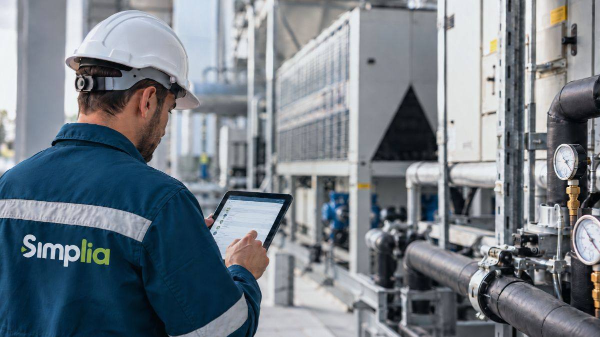 Técnico de mantenimiento con uniforme de Simplia inspecciona instalaciones y equipos industriales con una tablet en una planta técnica.